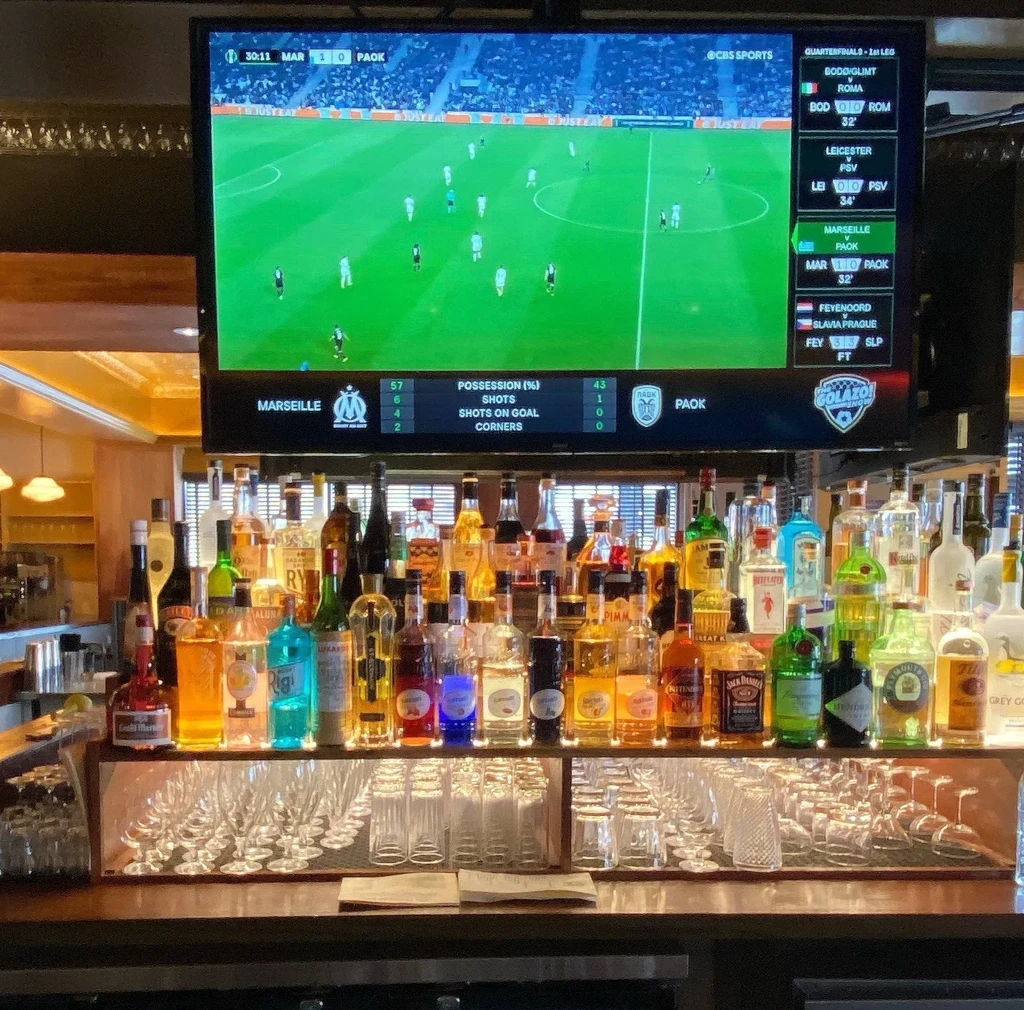 Well-stocked bar counter with a soccer match playing on the TV.