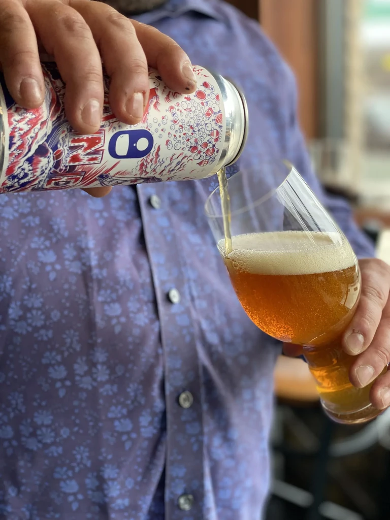 Hands pouring golden beer from a colorful can into a glass.