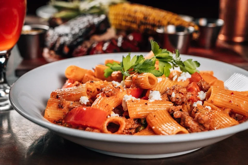 Close-up of rigatoni pasta with meat sauce, cheese, and parsley.