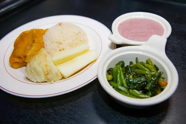 A meal with rice, stew, potatoes, cassava, purple soup, and greens.