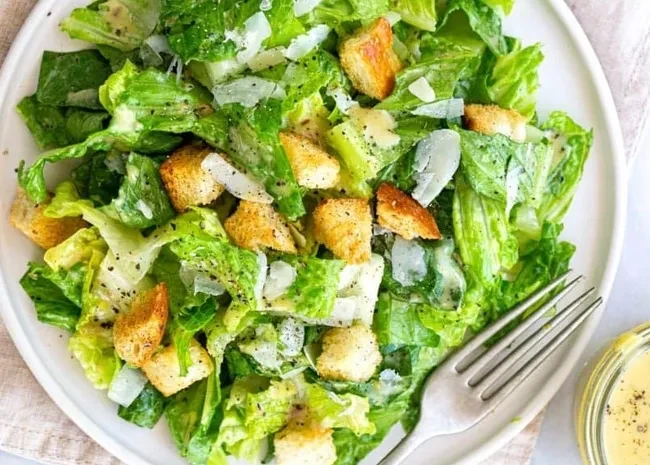 Caesar salad with romaine, croutons, Parmesan, dressing, and a fork.