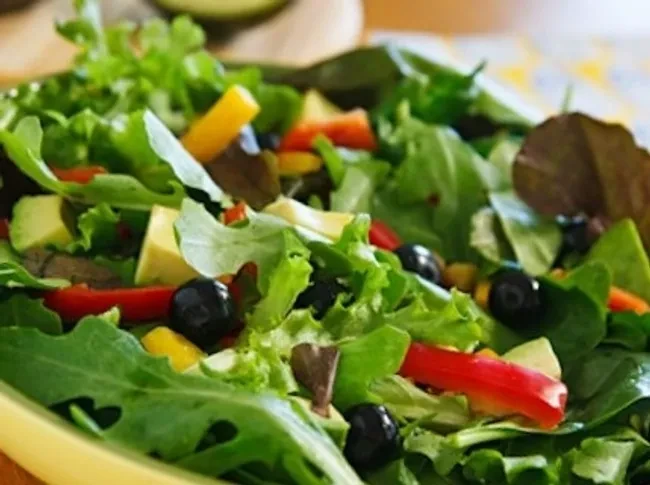 Bowl of colorful salad with leafy greens, peppers, and olives.
