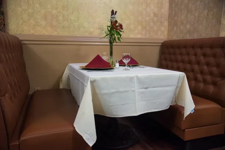 Restaurant booth table with white cloth, red napkins, flowers, brown leather seats.