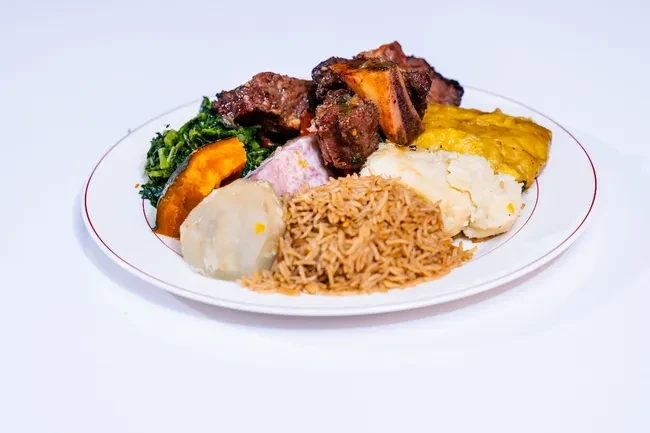 White plate of rice, stewed meat, leafy greens, and root vegetables.