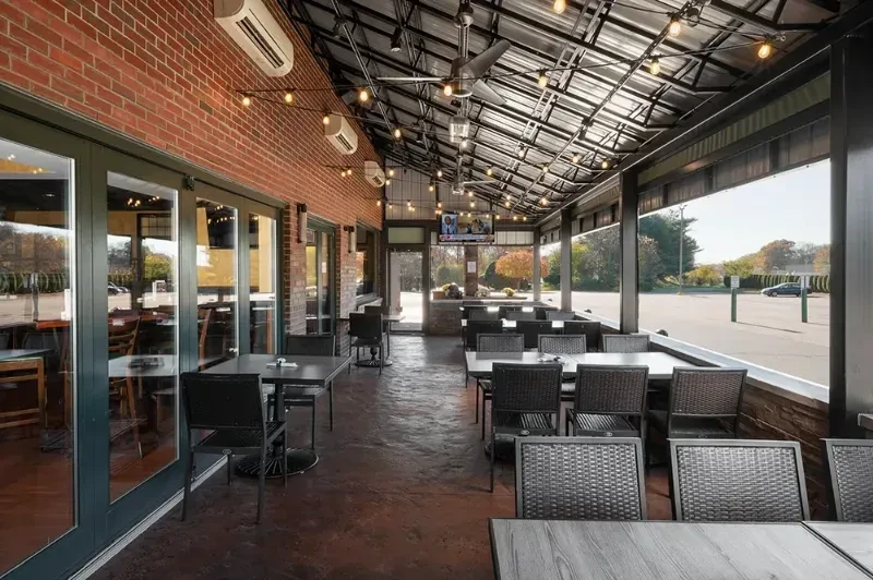 Restaurant patio with brick wall, corrugated roof, string lights, and seating.