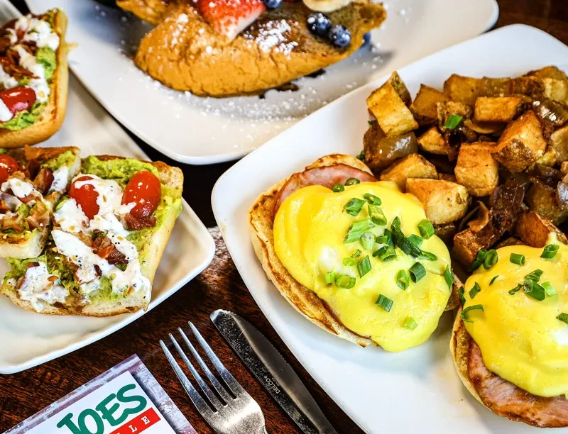 Avocado toast, Eggs Benedict, potatoes, and French toast on a wooden table.