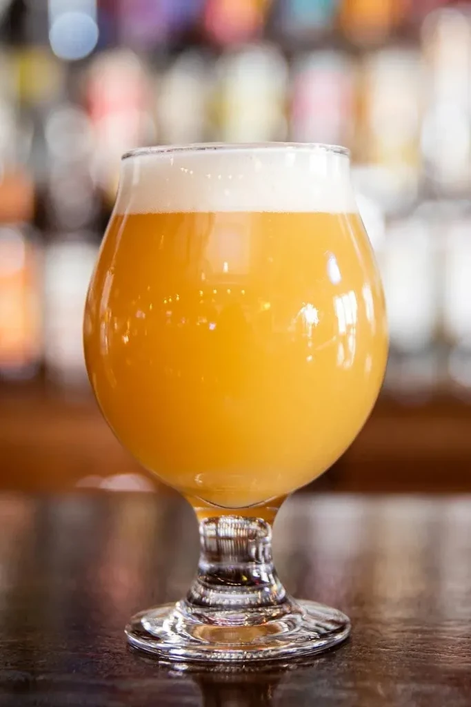 Hazy orange beverage in a goblet glass on a dark, reflective surface.