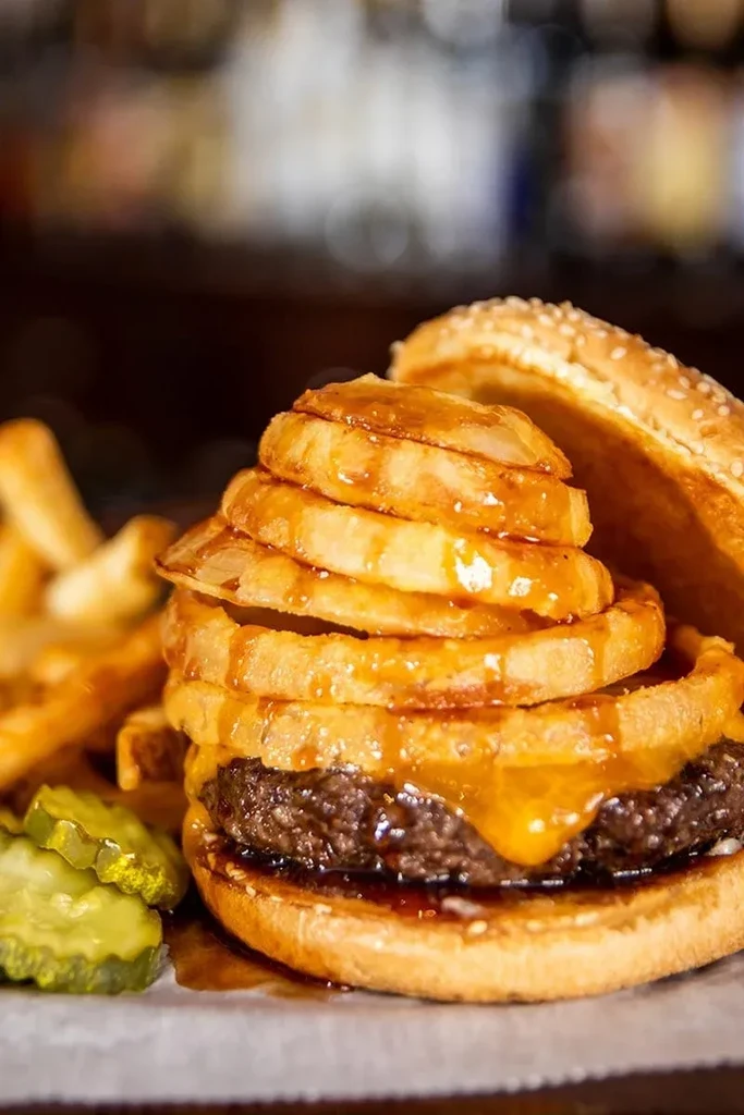 Gourmet burger with sauce-drizzled onion rings, fries, and pickles.