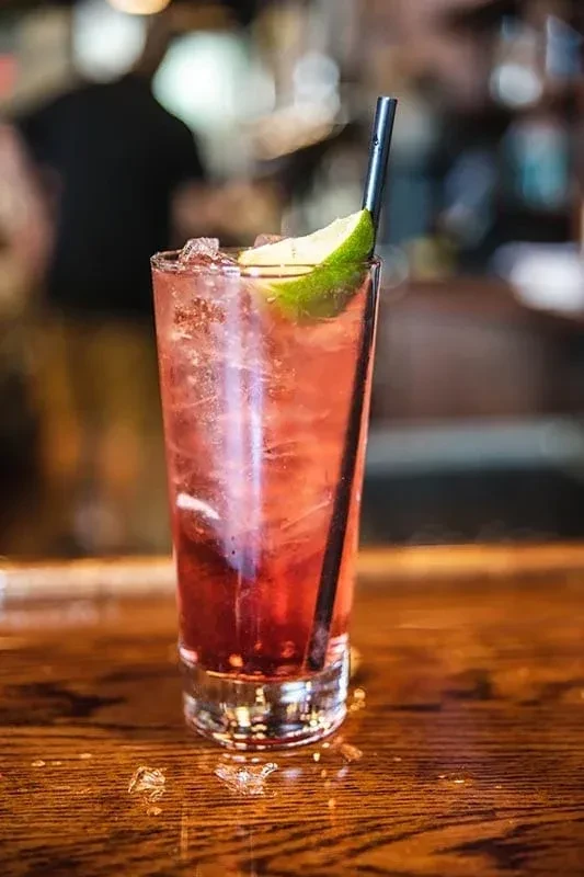 Iced red beverage with lime and straw on a bar top.