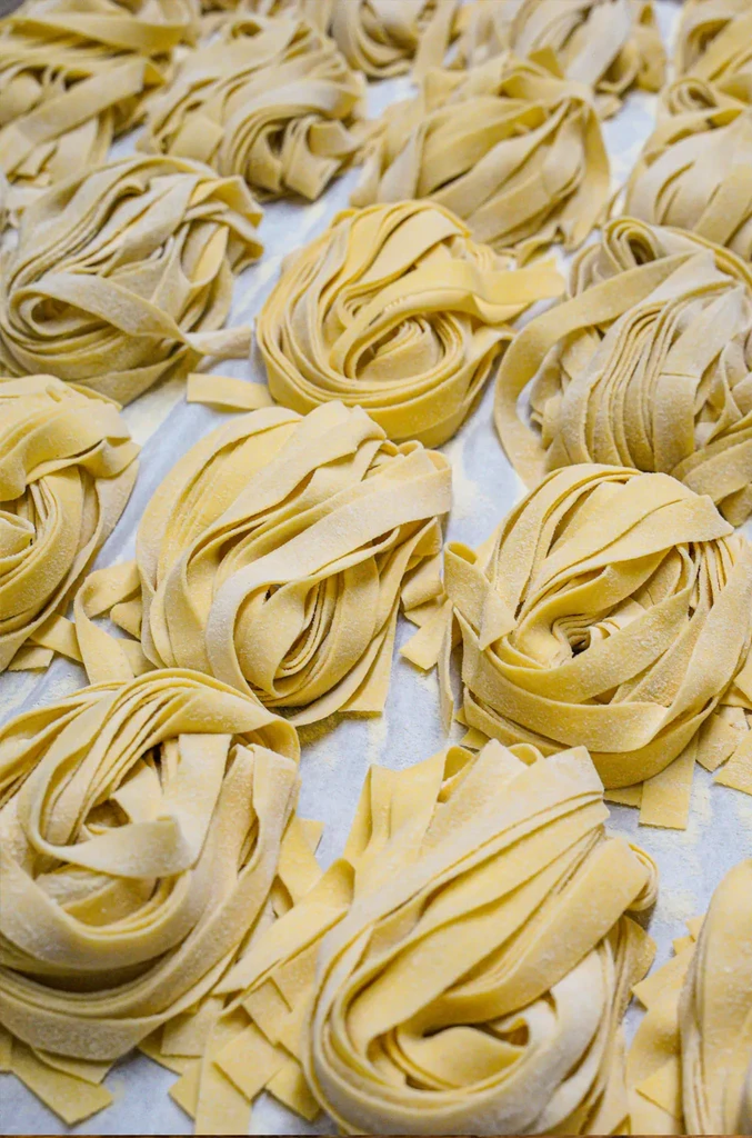 Numerous coiled nests of fresh, uncooked, flour-dusted egg pasta.