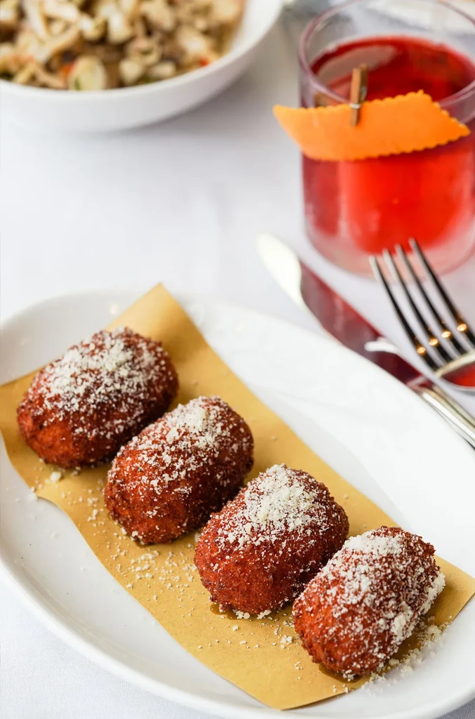 Four croquettes with Parmesan, garnished red drink, restaurant table.