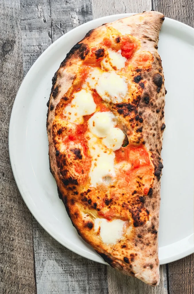 Rustic half-folded pizza or calzone with sauce, melted cheese, leopard-spotted crust.