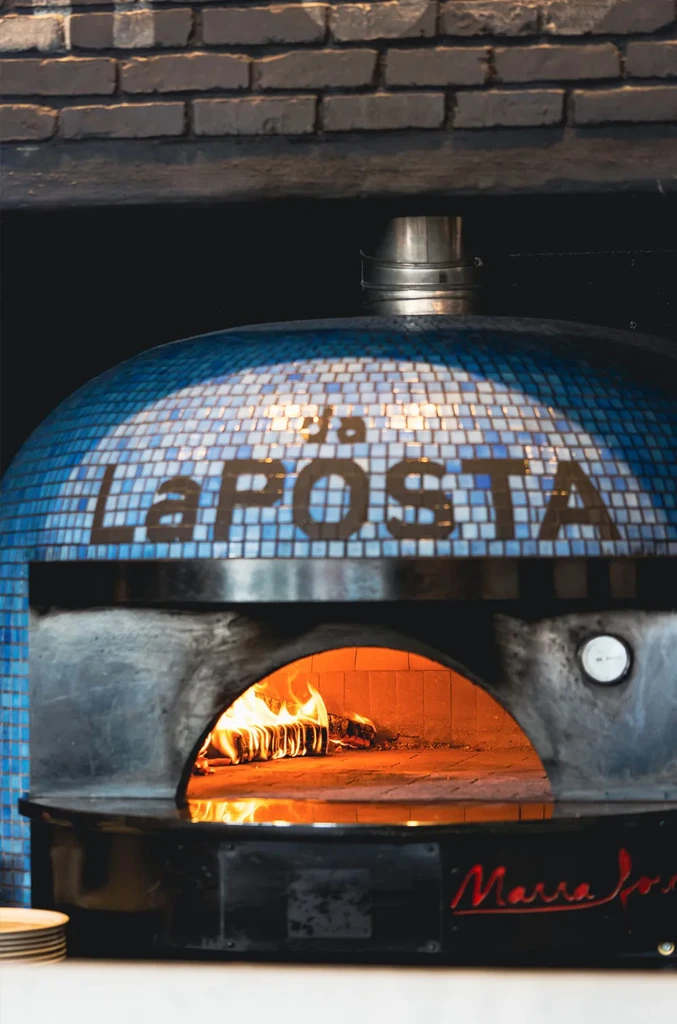 Blue mosaic wood-fired pizza oven "Da La POSTA" with roaring fire.