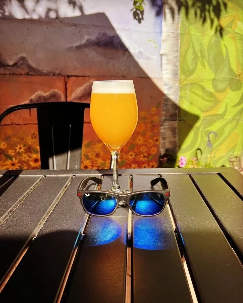 Hazy drink, blue sunglasses reflect on table, vibrant art wall.