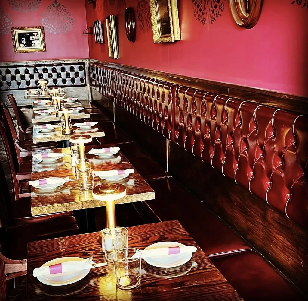 Warm restaurant interior with red booths, patterned wall, and gold lamps.