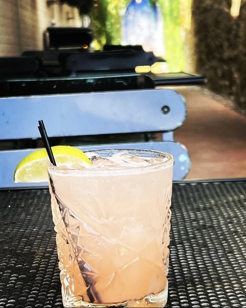Pinkish-orange cocktail in textured glass with lime, straw, and ice.