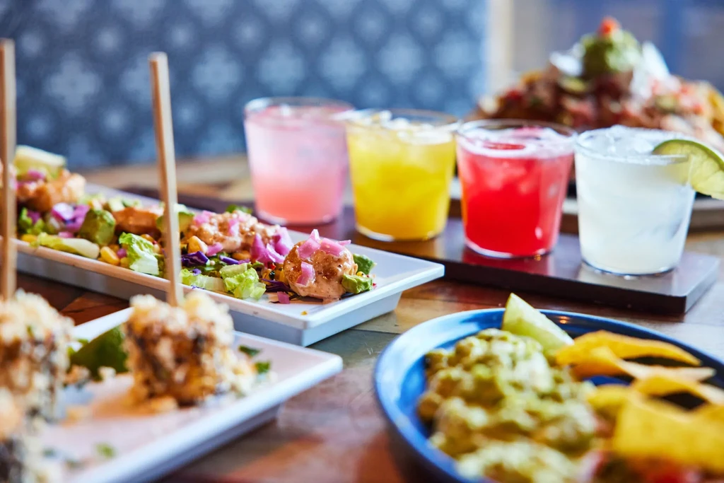 Colorful appetizers, guacamole, chips, and drinks on a rustic wooden table.