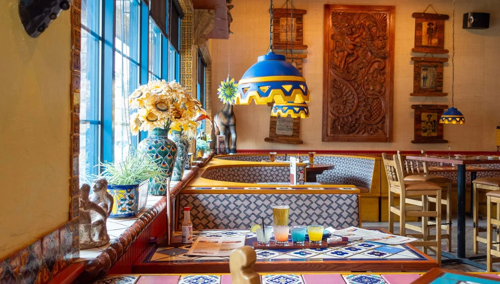 Colorful, sunlit restaurant interior with tiled table, drinks, and decor.