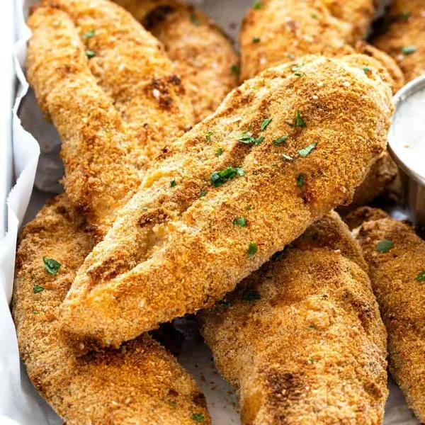 Crispy golden-brown breaded food piled with green herbs and dipping sauce.