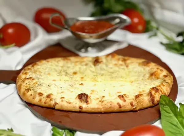 Cheesy flatbread on a wooden board with marinara, tomatoes, and herbs.