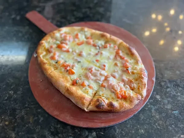 Thin-crust pizza with cheese, tomatoes, herbs on a wooden peel.