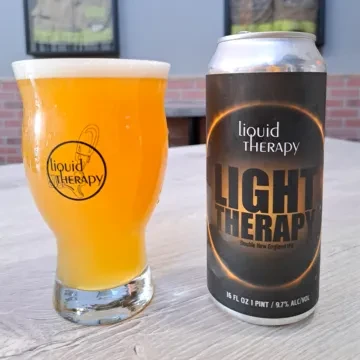 New England IPA in glass and "Light Therapy" can on a table.