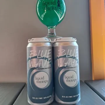 Two liquid THERAPY beer cans with a green glass on top.
