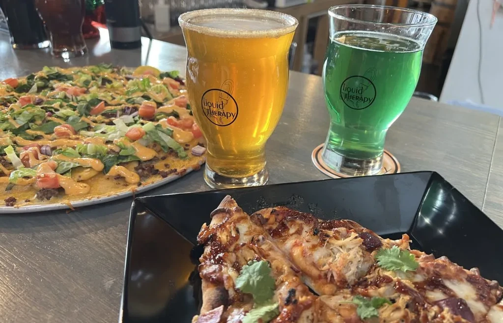 Overhead view of two pizzas and two 'Liquid Therapy' drinks.