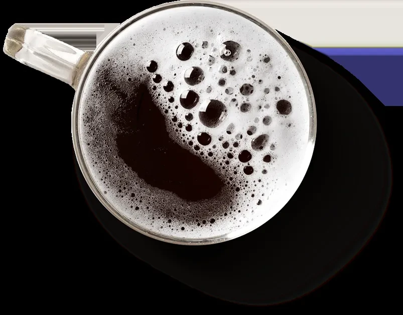 Top-down, dark beverage in glass mug with thick white foam.