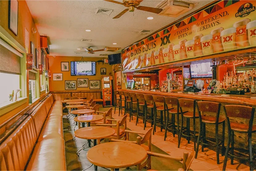 Empty, warm-lit restaurant interior with a bar and booth seating.