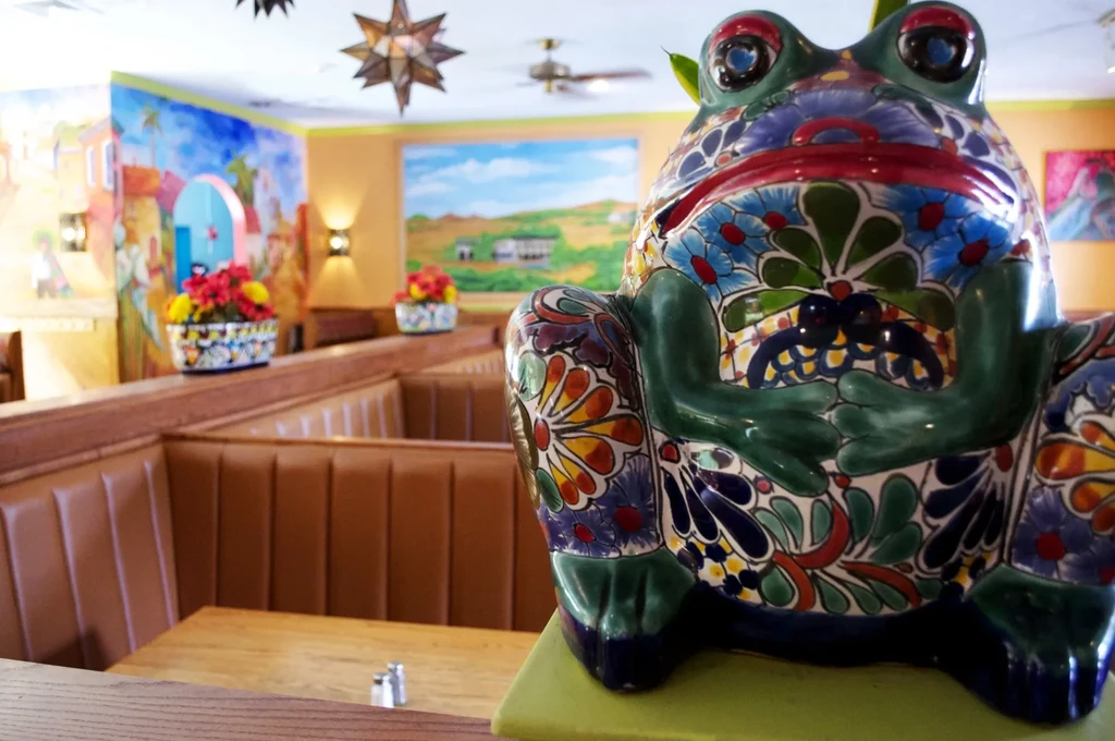 Large colorful Talavera frog statue in a restaurant with vibrant murals.