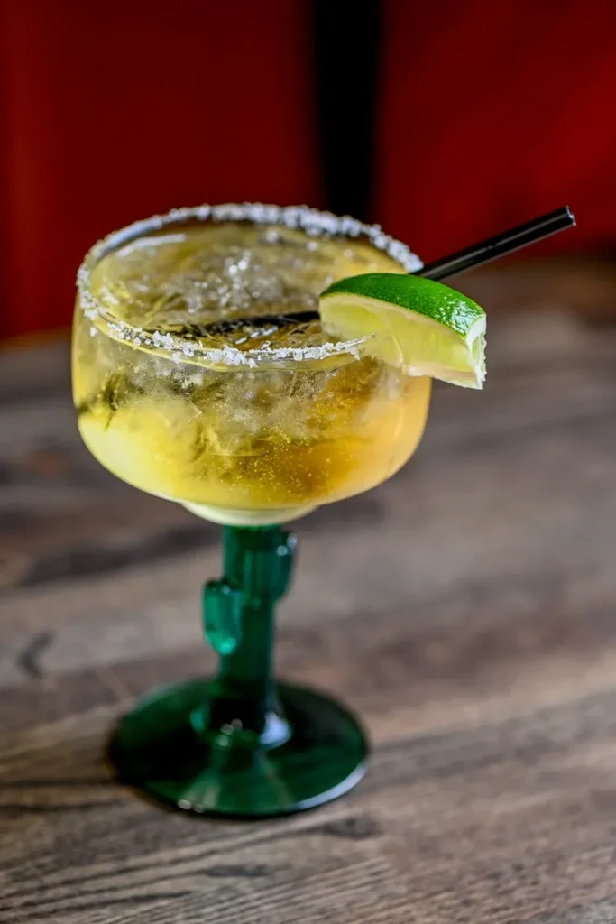 Pale green margarita in cactus glass with salted rim and lime.