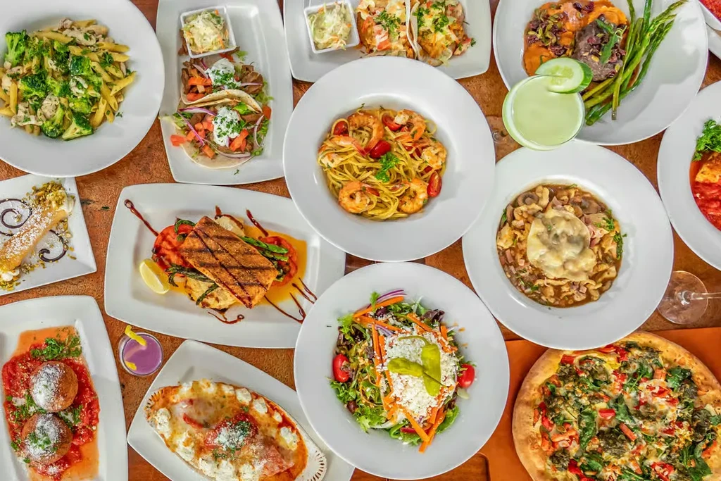 Flat lay of numerous diverse dishes and cocktails on a wooden table.