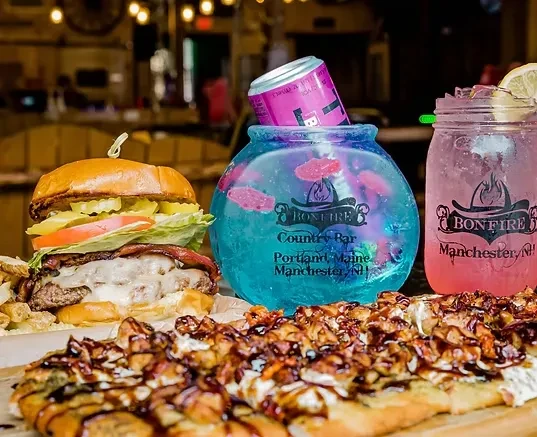 Burger, flatbread, blue and pink Bonfire branded drinks on wood.