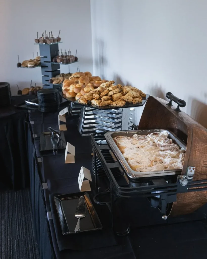 Buffet table laden with desserts, baked goods, and frosted cinnamon rolls.