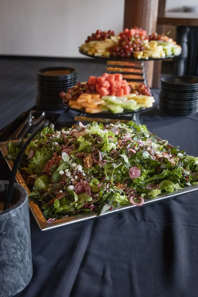 Buffet with large salad, feta, nuts, and tiered fresh fruit platters.