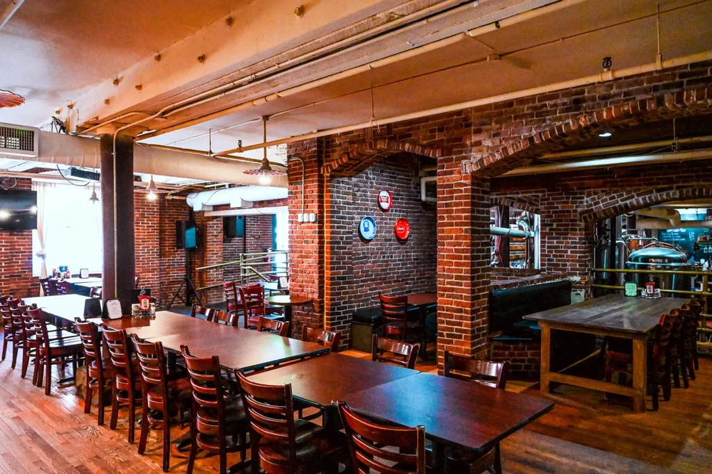 Empty rustic-industrial brewpub interior with long tables and brewing tanks.