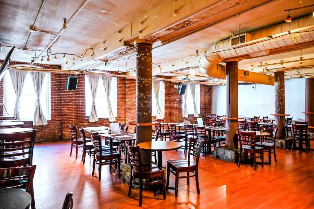 Empty industrial-style dining room with wooden tables, brick walls, string lights.