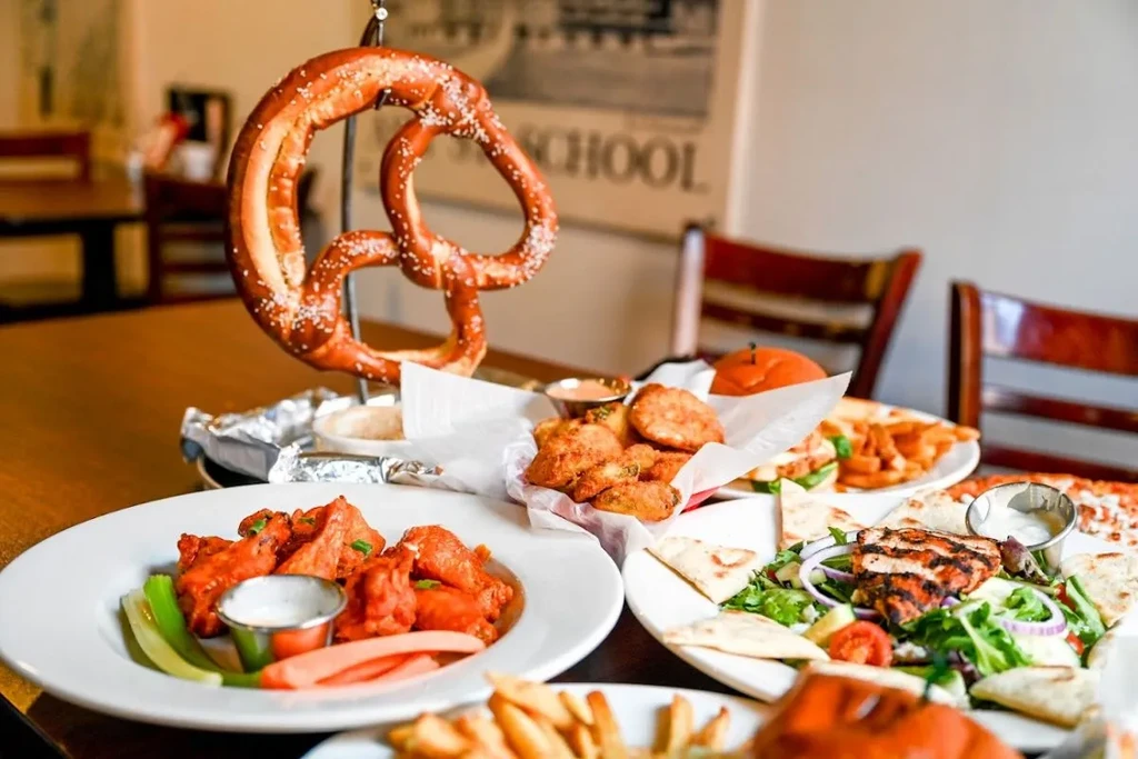 A pretzel, buffalo wings, chicken salad, and fried appetizers on a table.