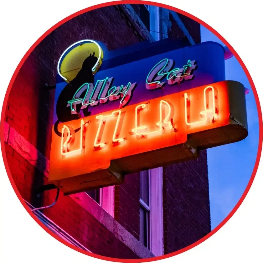 Neon sign for Alley Cat Pizzeria with a cat on a crescent moon.