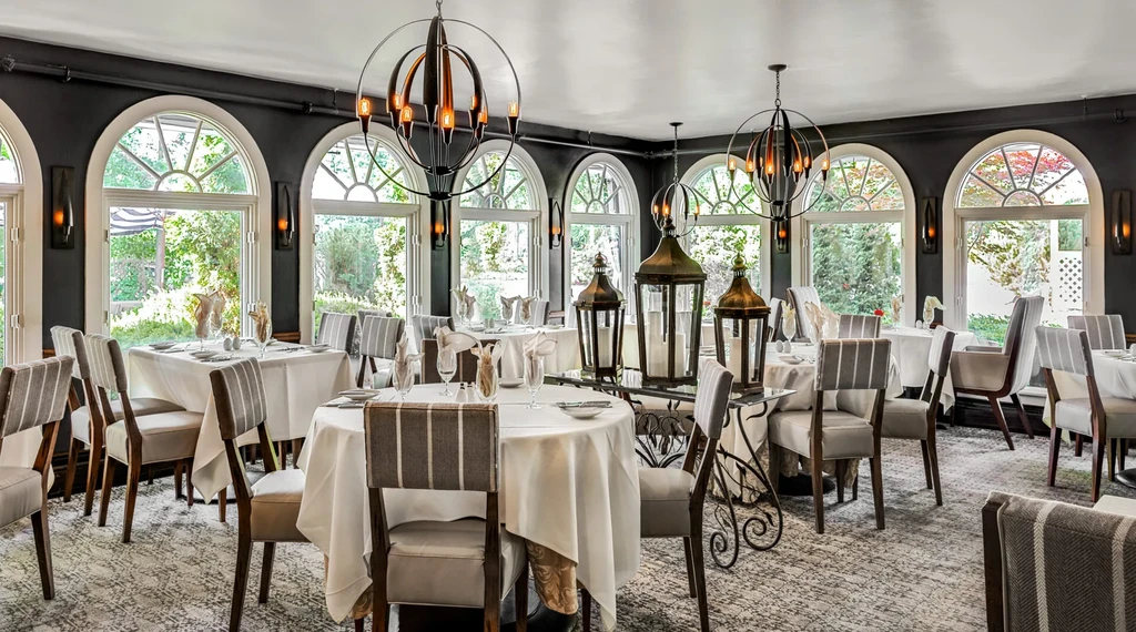 Elegant, empty restaurant dining room; set tables, arched windows, modern chandeliers.