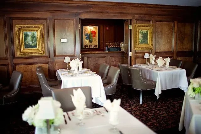 Dark wood paneled dining room with set tables and a lighted bar.