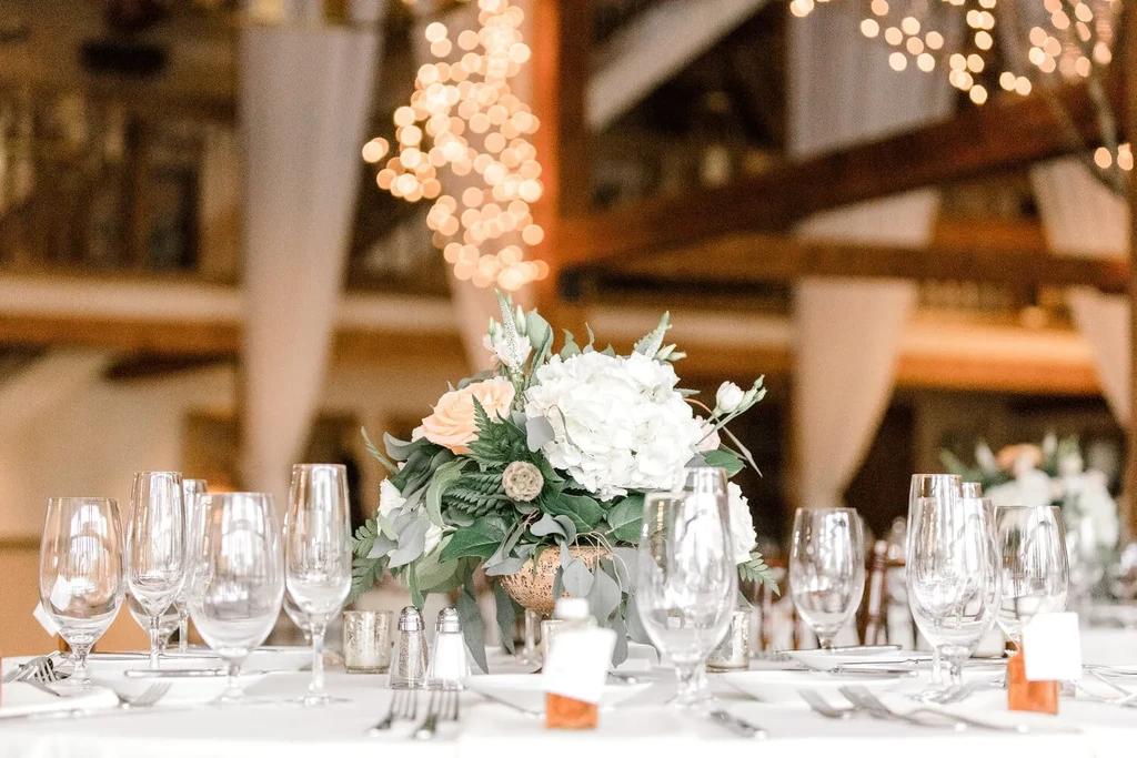 Elegant dining table with peach and white flowers, gold vase, string lights.