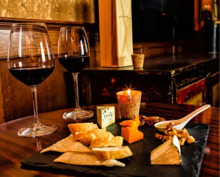Red wine glasses, cheese board, baguette, walnuts, and a lit candle.