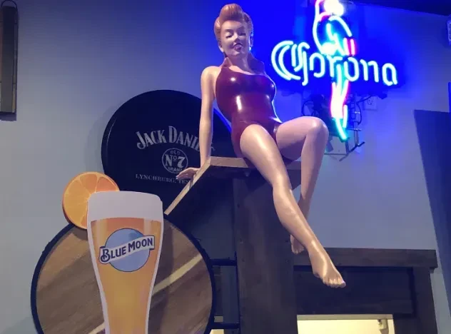 Dimly lit bar with red-haired mannequin and multiple branded signs.