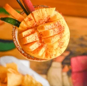 Overhead view of a vibrant drink with fanned mango, chili, and lime.