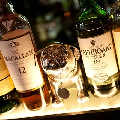 Macallan and Laphroaig Scotch bottles with a silver pug on a bright shelf.