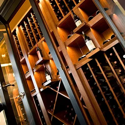 Extensive wooden wine cellar filled with numerous, illuminated wine bottles.
