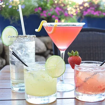 Four colorful mixed drinks with garnishes on an outdoor patio table.