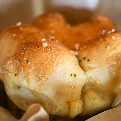 Glossy golden-brown bread rolls sprinkled with salt and herbs in a basket.